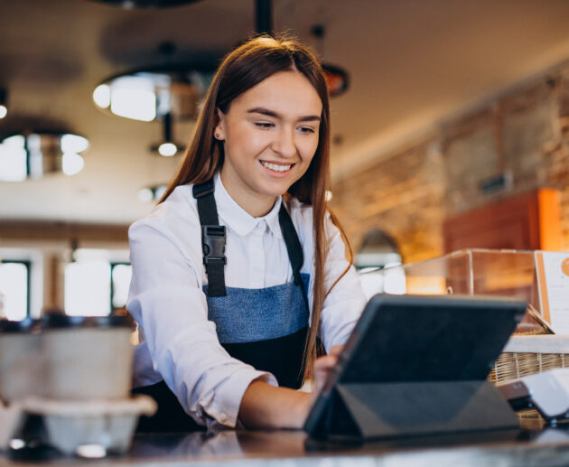 mulher de avental utilizando um chatbot para restaurante através de um tablet em um balcão