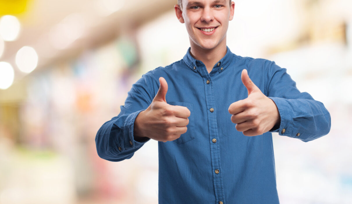 homem branco, cabelos loiros, camisa social da cor azul, levantando os polegares em sinal de aprovação / satisfação dos clientes